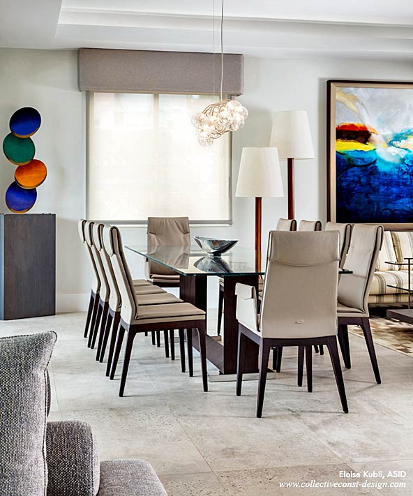 A smoked-oak dining table base supports a double-bevel crystal clear glass top, and is surrounded by eight tall leather side chairs. A colorful metal Coin Toss sculpture is displayed on a custom pedestal. A pair of two-tiered floor lamps connects the Dining Room to the Living Room.