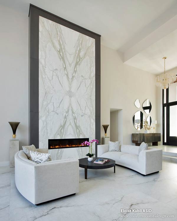 A linear gas fireplace is framed by four floor-to-ceiling book-matched marble slabs. The entire 22-foot-high installation is wrapped in white oak.