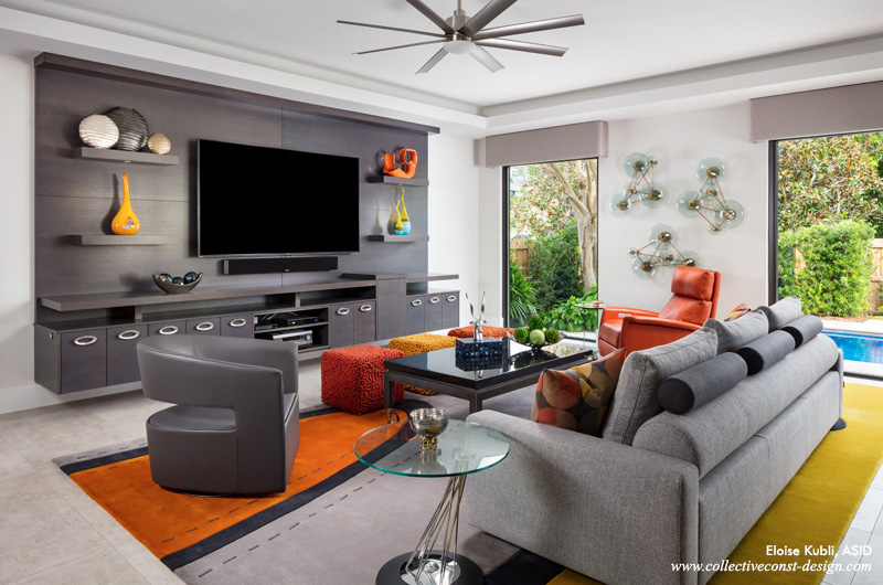 A suspended gray, rift-cut oak wall unit with an 85-inch TV screen and lighting beneath is the centerpiece of the family room.